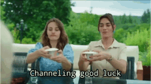 two women are sitting at a table with cups in their hands and the caption says channeling good luck .