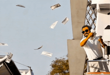 a man on a boat talking on a phone with money flying around him