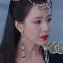 a woman wearing a tiara and earrings is looking at the camera .