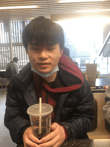 a young man wearing a mask is holding a cup of soda