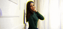 a woman in a green sweater is standing in front of a window and smoking a cigarette .