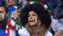 a woman wearing an afro wig and a wreath of flowers is watching a soccer game between italy and croatia