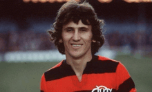 a man in a red and black striped shirt is standing on a soccer field .