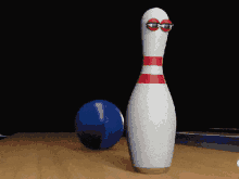 a bowling pin with googly eyes is standing next to a blue ball