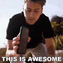 a man holding a cell phone with the words " this is awesome " on the bottom