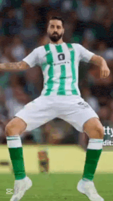 a soccer player wearing a green and white striped jersey and green socks is dancing on the field .