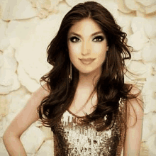 a woman in a gold sequined top is standing in front of a wall .