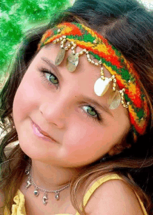 a little girl wearing a colorful headband and a necklace smiles for the camera