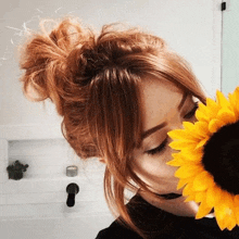 a woman with red hair is holding a sunflower in her mouth