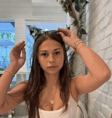 a woman in a white tank top has her hands on her head