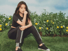 a woman wearing black adidas pants sits on a grassy hill