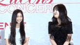 two young women are standing next to each other and smiling in front of a sign that says concert .