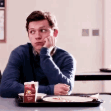 a young man is sitting at a table with a tray of food and a box of borden juice .