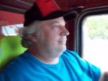 a man wearing a blue shirt and a red hat with the word labrador on it looks out a window