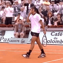 a man is walking on a tennis court holding a tennis racquet in front of a cafe de colomb sign