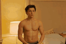 a shirtless man is standing in a bedroom next to a bed .