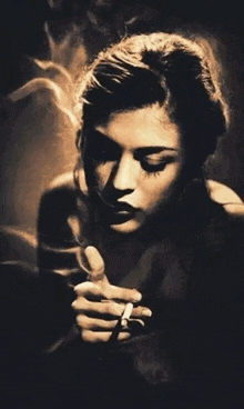 a woman is smoking a cigarette in a dark room in a black and white photo .