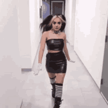 a woman is walking down a hallway wearing a black leather dress and boots .