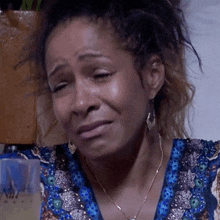 a woman with tears running down her face is wearing a blue shirt and earrings .