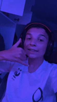 a boy wearing headphones and a white shirt with a rooster on it giving a thumbs up