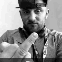 a man wearing a hat and a lanyard is giving the middle finger in a black and white photo .