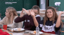 a group of young women are sitting at a table with plates of food and a bottle of water .