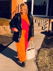 a woman in a pink and orange outfit is standing on a sidewalk holding a white tote bag .