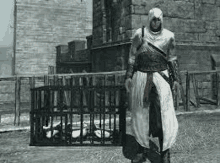 a man in a white robe and hood is standing in front of a cage .