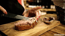 a person is cutting a piece of bread with a knife on a wooden cutting board with trendizisst written on it