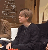 a man in a striped sweater is sitting on a couch with a christmas tree in the background .