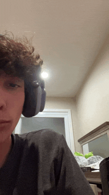 a young man with curly hair wearing headphones looks at the camera