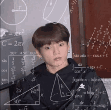 a young man is sitting in front of a chalkboard with a lot of math equations on it .