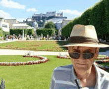 a man wearing a hat and sunglasses is standing in front of a park .