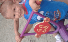 a little boy wearing a blue shirt with cars on it is riding a purple toy