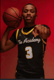 a man in a the academy jersey is holding a basketball and pointing at the camera