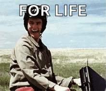 a man wearing a helmet is sitting in a field holding a briefcase with the words for life written above him