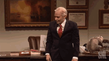 a man in a suit and tie is standing in front of a desk with a framed diploma from the university of alabama