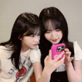 two girls are looking at a pink cell phone .