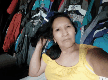 a woman in a yellow tank top is standing in front of a wall of clothes