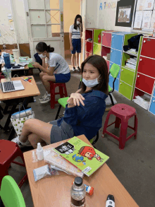 a girl wearing a mask sits at a desk with a book that says a thorn