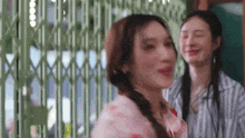 a couple of women are standing next to each other in front of a green gate .