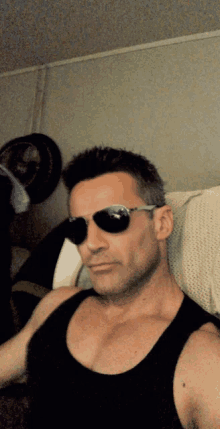 a man wearing sunglasses and a black tank top looks at the camera