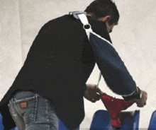 a man wearing a black jacket and blue jeans is holding a red thong