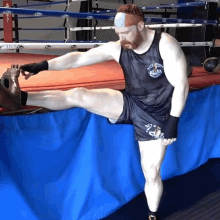 a man stretches his leg in a boxing ring wearing a black tank top that says ' boxing club ' on it