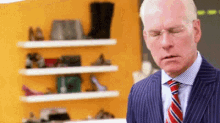 a bald man in a suit and tie is standing in front of a shelf with shoes on it .