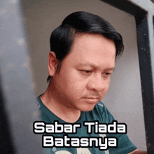 a man wearing a green shirt with the words " sabar tiada batalsnya " on the bottom