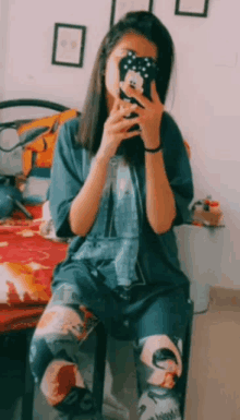 a girl is sitting on a chair taking a picture of herself with her cell phone .