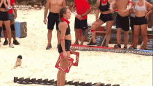 a group of people are standing on a beach and one of them is wearing a red bandana on her neck