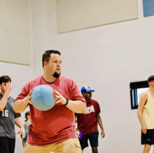 a man in a red shirt is holding a blue ball in his hands