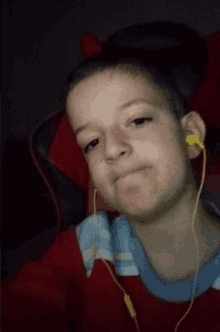 a young boy wearing a red shirt and yellow ear buds looks at the camera